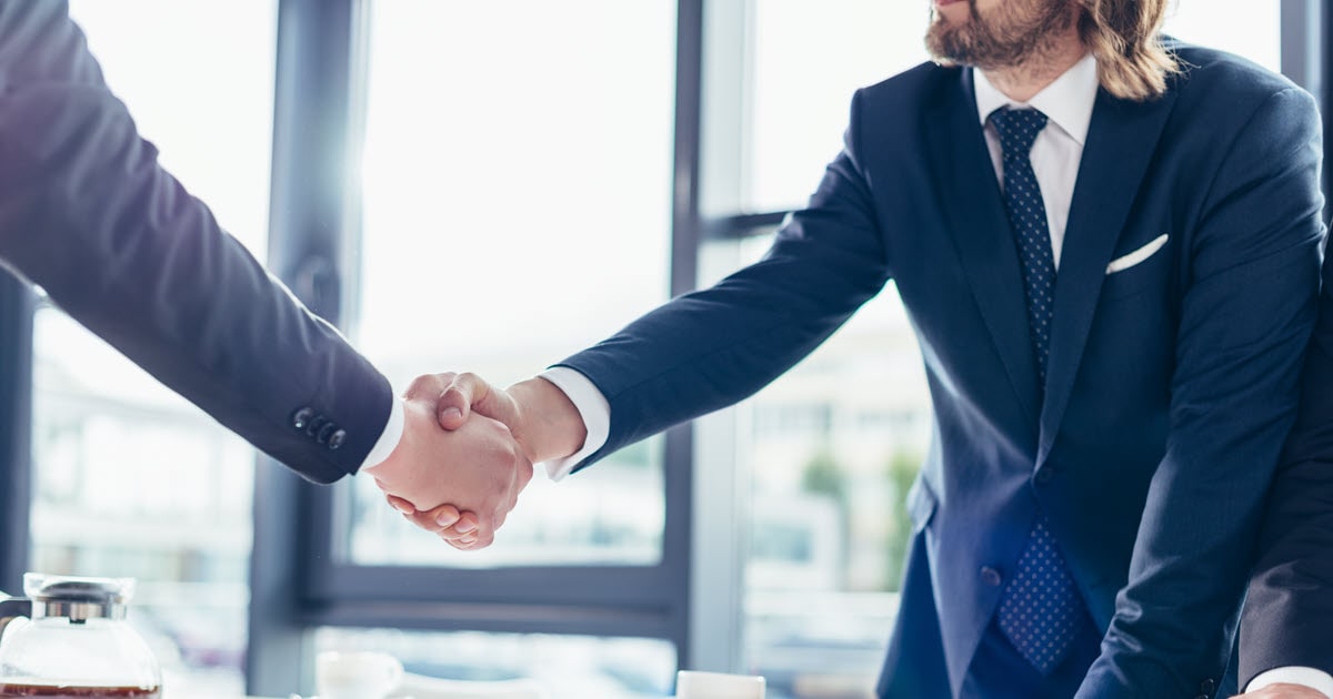 Two businessmen signing partnership agreement and shaking hands.