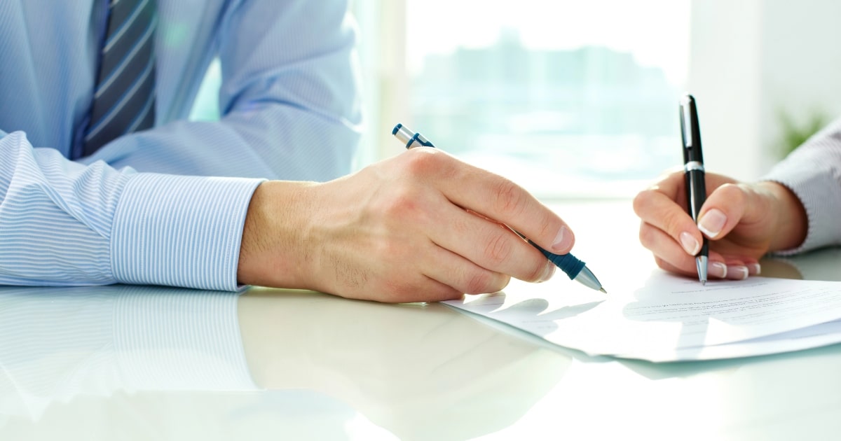 Close up view of hands signing a document, depicting a business sale agreement.